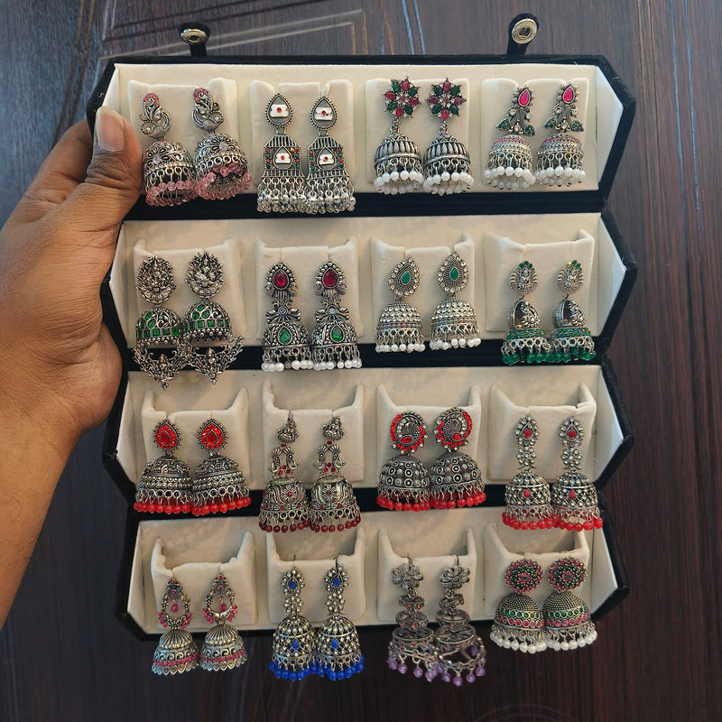 Hand holding an open black velvet box with 16 pairs of oxidised silver jhumka earrings – Jaan Creations