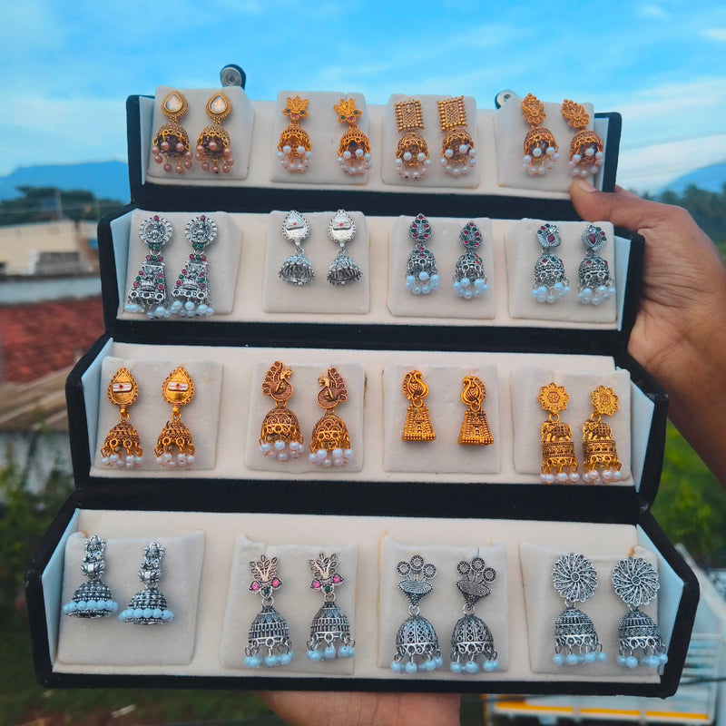 Hand holding an open black velvet box with 16 pairs of antique gold and oxidised silver temple jhumka earrings – Jaan Creations
