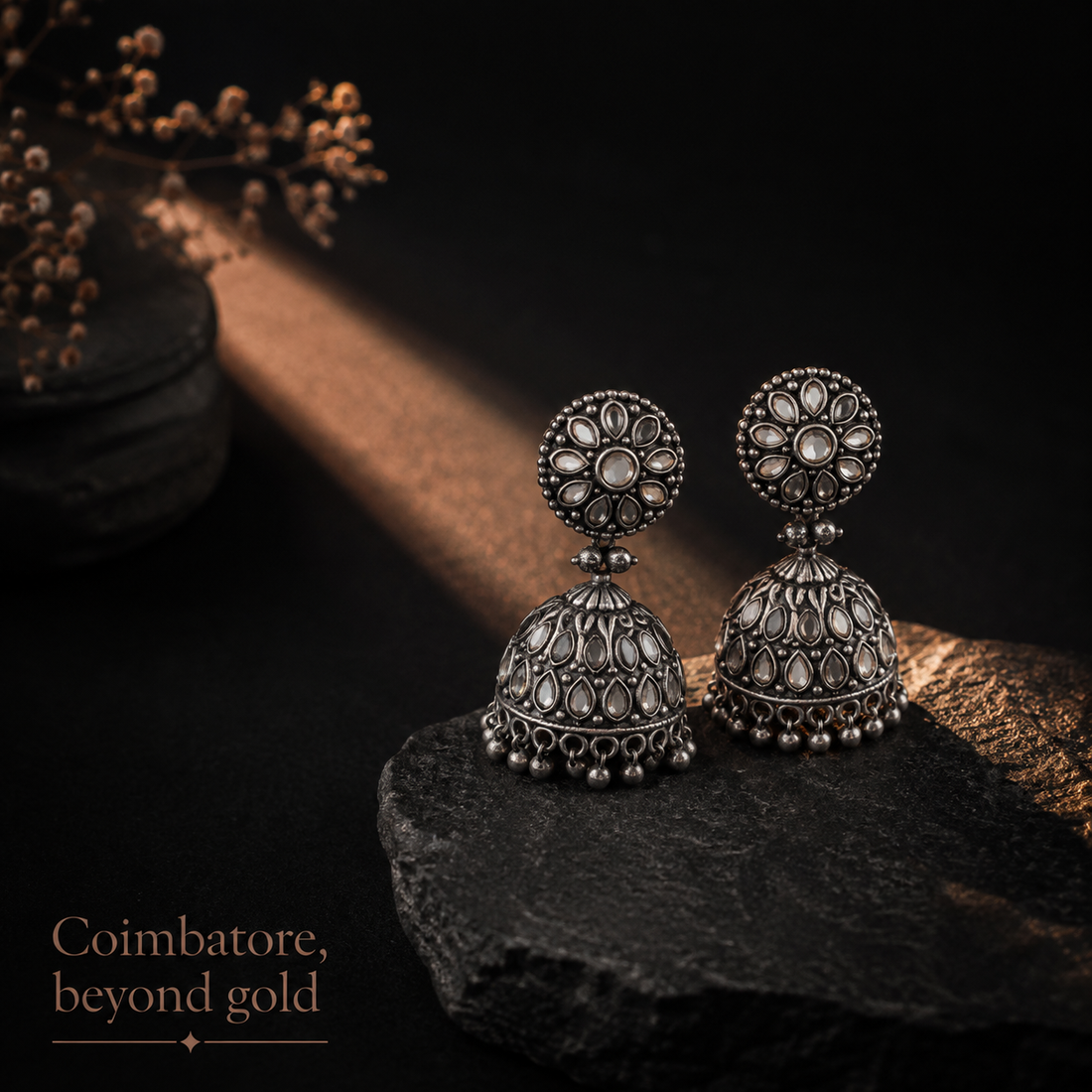 Oxidised silver jhumka earrings resting on dark stone in a shaft of warm light