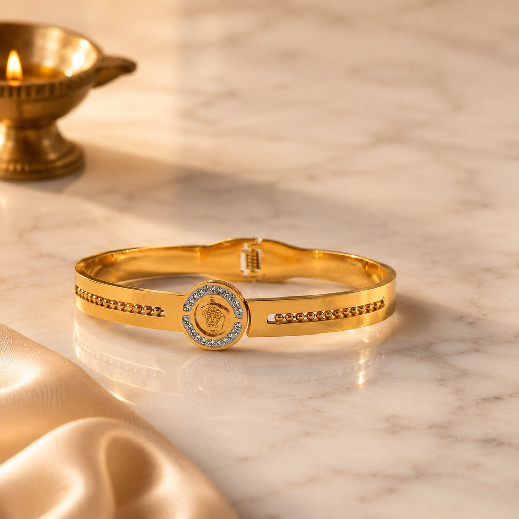 Gold-plated hinged bangle bracelet with a stone-set medallion, displayed on a white marble surface