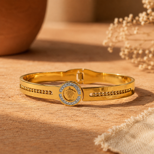 Gold-plated bangle bracelet with a crystal-set medallion centrepiece, resting on a wooden surface