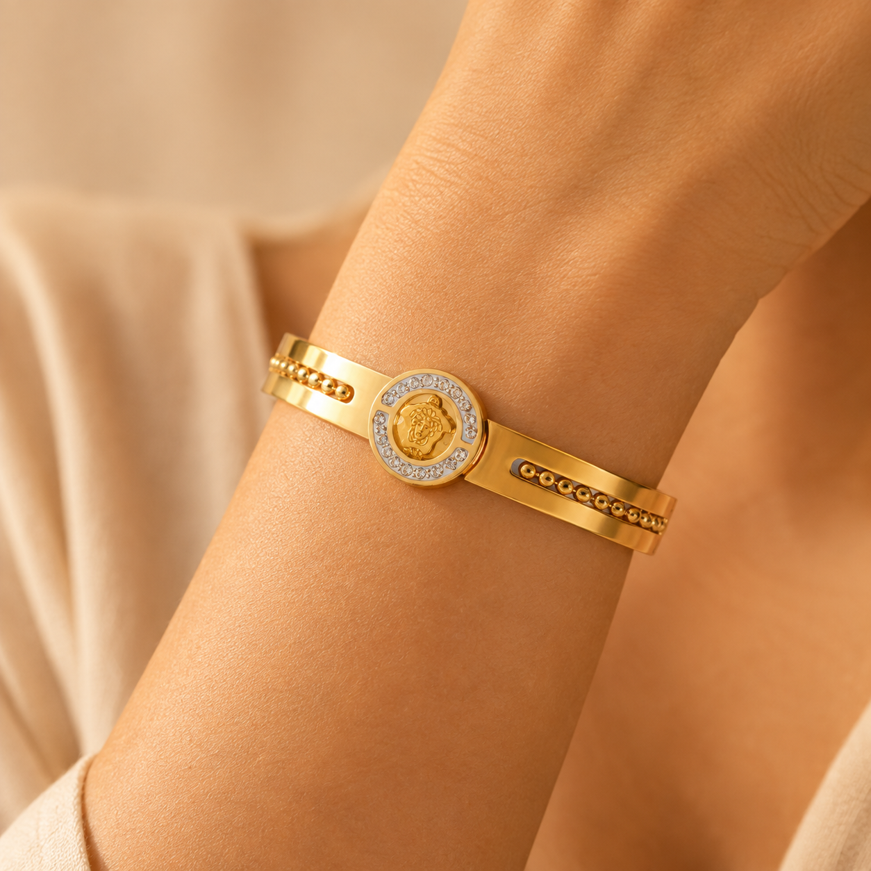 Close-up of a gold-plated medallion bangle bracelet with crystal detailing worn on a wrist