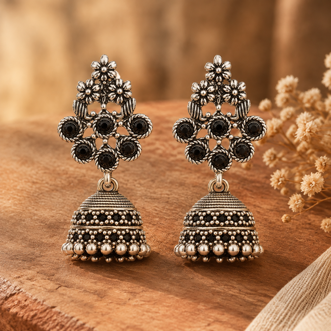 Oxidised silver floral jhumka earrings with black stones on wooden surface
