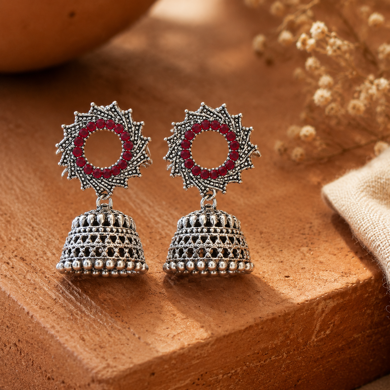 Oxidised silver sunburst jhumka earrings with red stones on terracotta