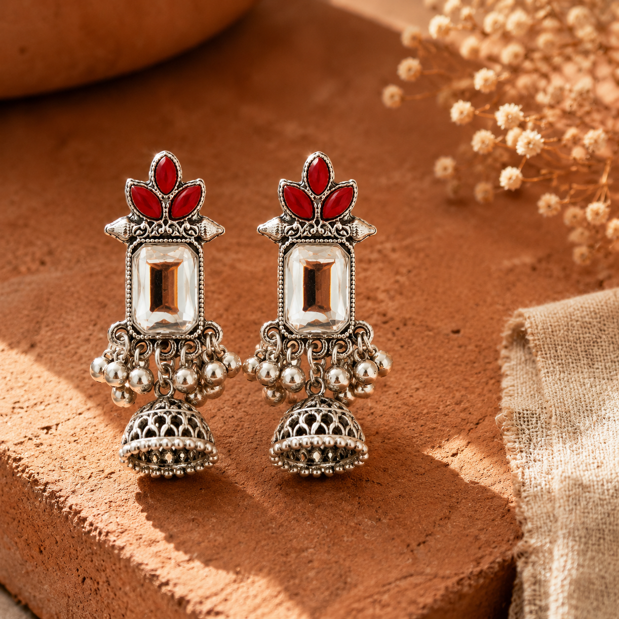 Oxidised silver red stone jhumka earrings styled on terracotta surface