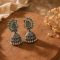 Oxidised silver peacock jhumka earrings with green stones on terracotta
