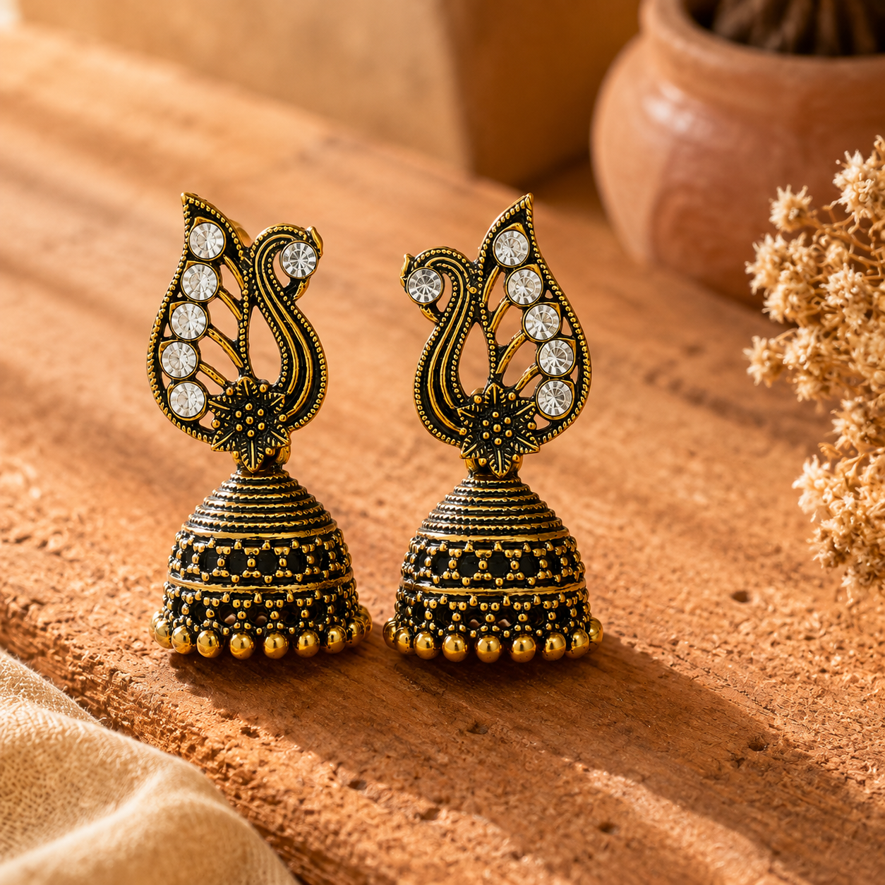 Antique gold peacock jhumka earrings styled on terracotta surface