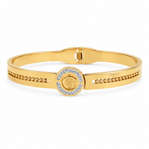 Gold-plated medallion bangle bracelet resting on a wooden surface