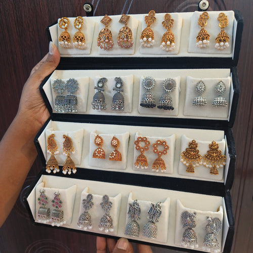 Hand holding an open black velvet box with 16 pairs of antique gold and oxidised silver jhumka earrings – Jaan Creations