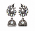 A pair of silver-toned Jhumka earrings featuring peacock motifs adorned with iridescent white and multicolor stones, hanging from ornate filigree bell-shaped drops on a plain white background.