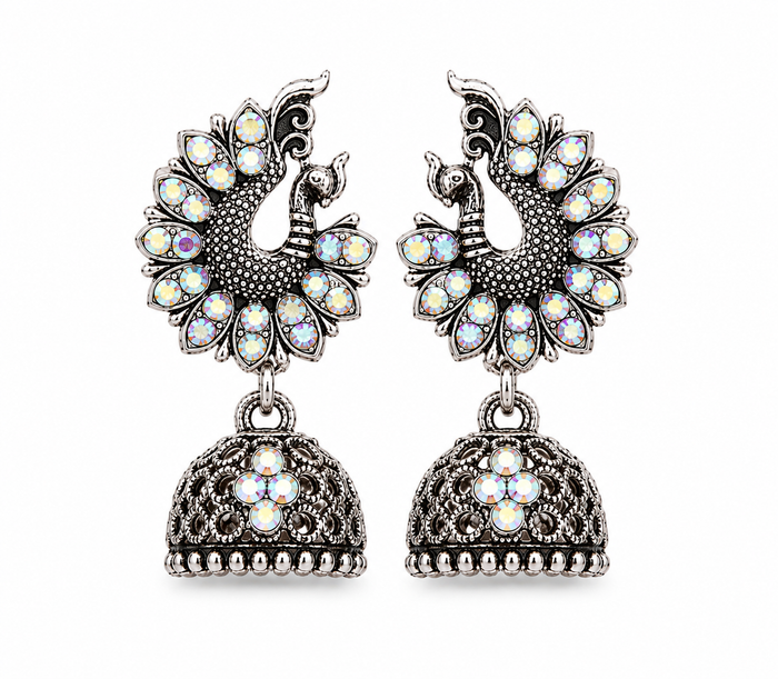 A pair of silver-toned Jhumka earrings featuring peacock motifs adorned with iridescent white and multicolor stones, hanging from ornate filigree bell-shaped drops on a plain white background.
