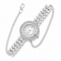 A silver-tone quartz watch with a round white dial, surrounded by a halo of clear crystals, and a wide crystal-embellished link bracelet with an attached curb chain clasp, shown on a white background.
